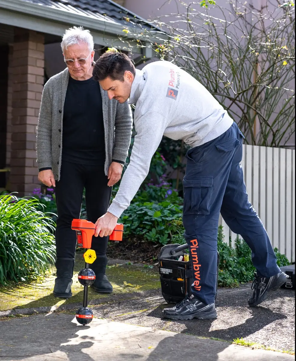 A Plumbwell plumber using leak detection equipment in a front yard